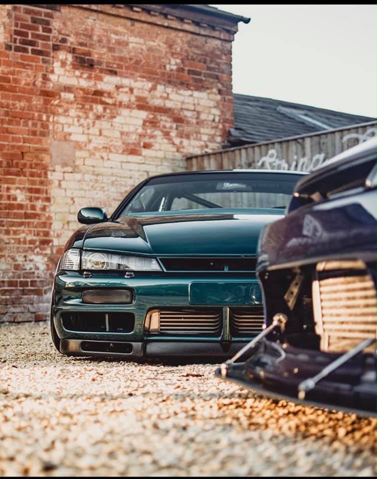 Two lowered coupes beside a weathered brick building