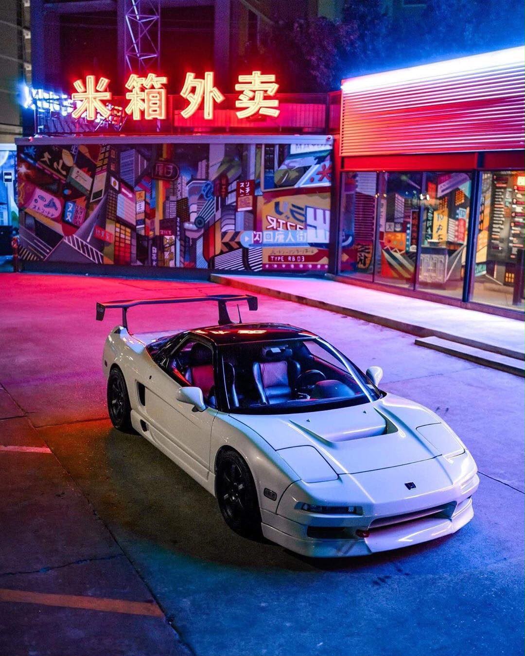 White Acura NSX beneath colorful neon signs at night